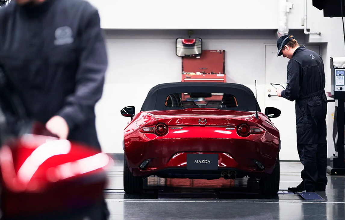 Rear view of Mazda Roadster as it gets inspected by mechanic in the workshop